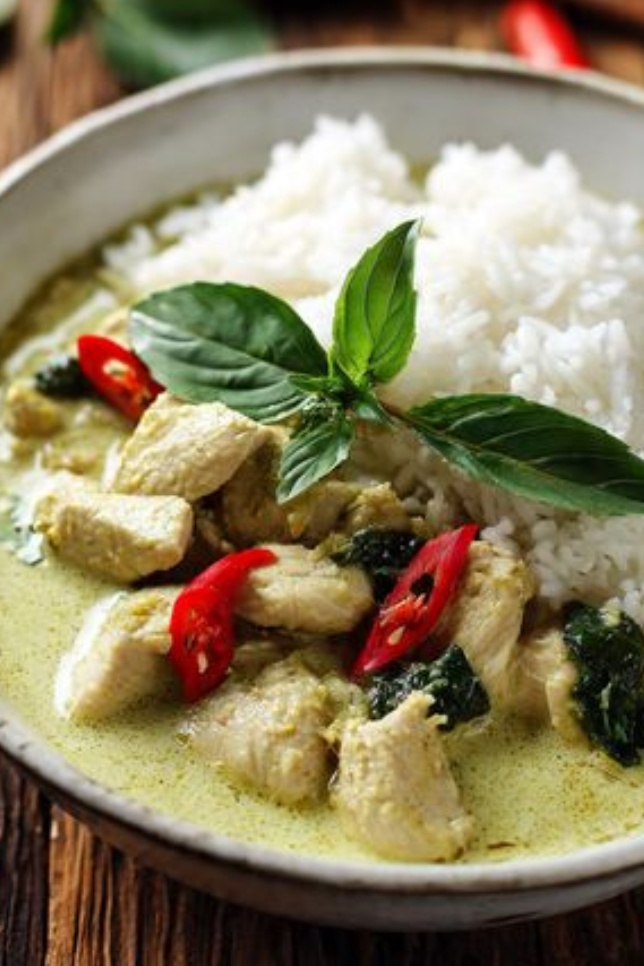Thai green curry chicken with tender meat in vibrant green coconut sauce, garnished with Thai basil and served over jasmine rice