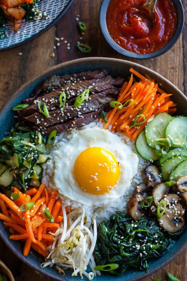 Colorful Korean bibimbap bowl with rice, vegetables, fried egg, and beef served with gochujang sauce