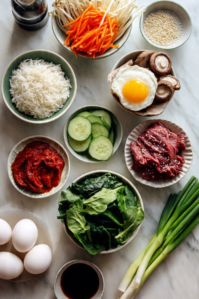 All ingredients needed to make Korean bibimbap bowl including rice, vegetables, beef, gochujang, and sesame oil